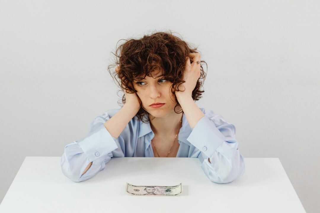 A white woman looks stressed with a cash note on the table in front of her