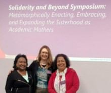 Three women smile at a camera with the text Solidarity and Beyond Symposium