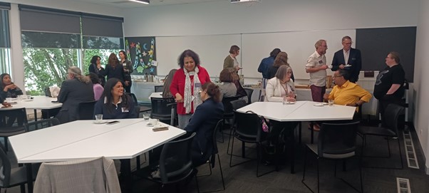 a classroom of people interacting with each other, some are seated at tables, others are standing