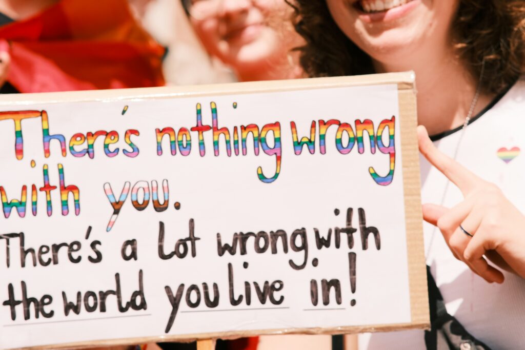 people hold a sign that reads (in pride colours) 'There's nothing wrong with you. There's a lot wrong with the world you live in!'