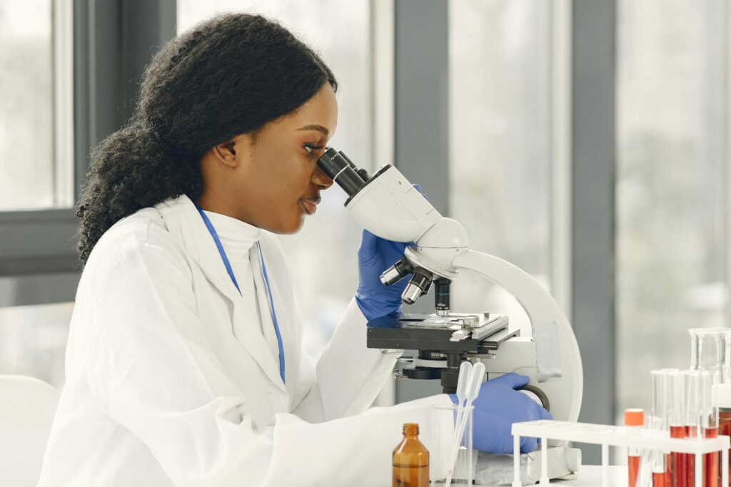 A Black woman scientist in a lab coat using a microscope in a modern laboratory setting