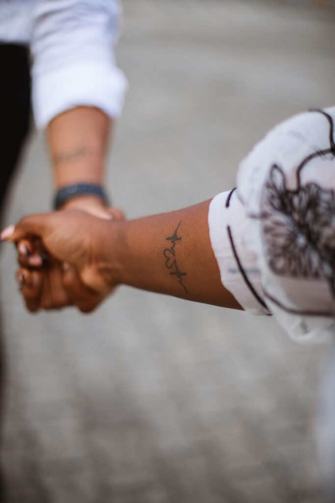 two hands holding each other, one has a tattoo of a heartbeat with a heart integrated into the design